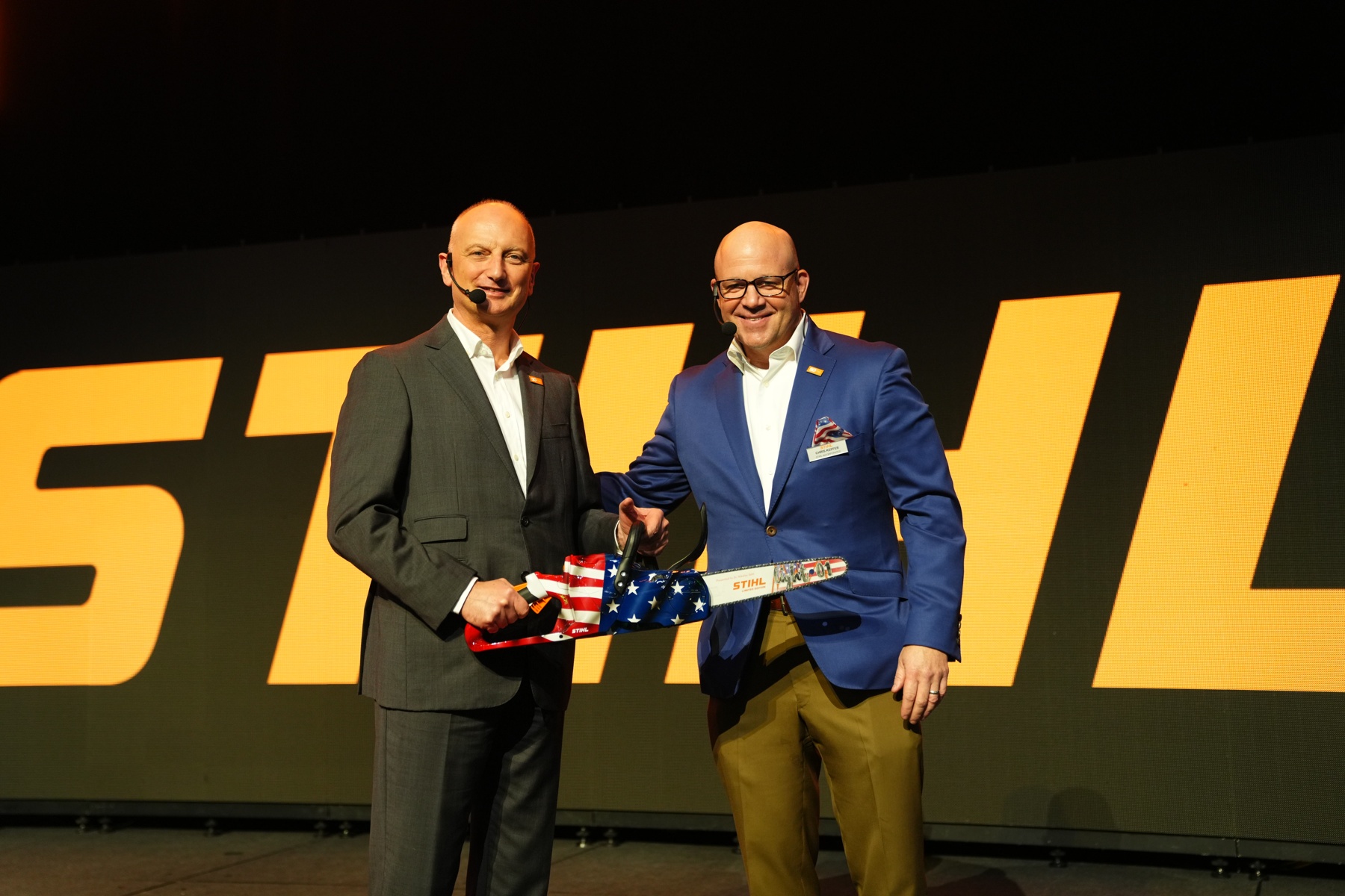 El Dr. Nikolas Stihl (izquierda) y Chris Keffer, Director General de STIHL Inc. en EE.UU., presentan una sierra de aniversario con una bandera estadounidense.